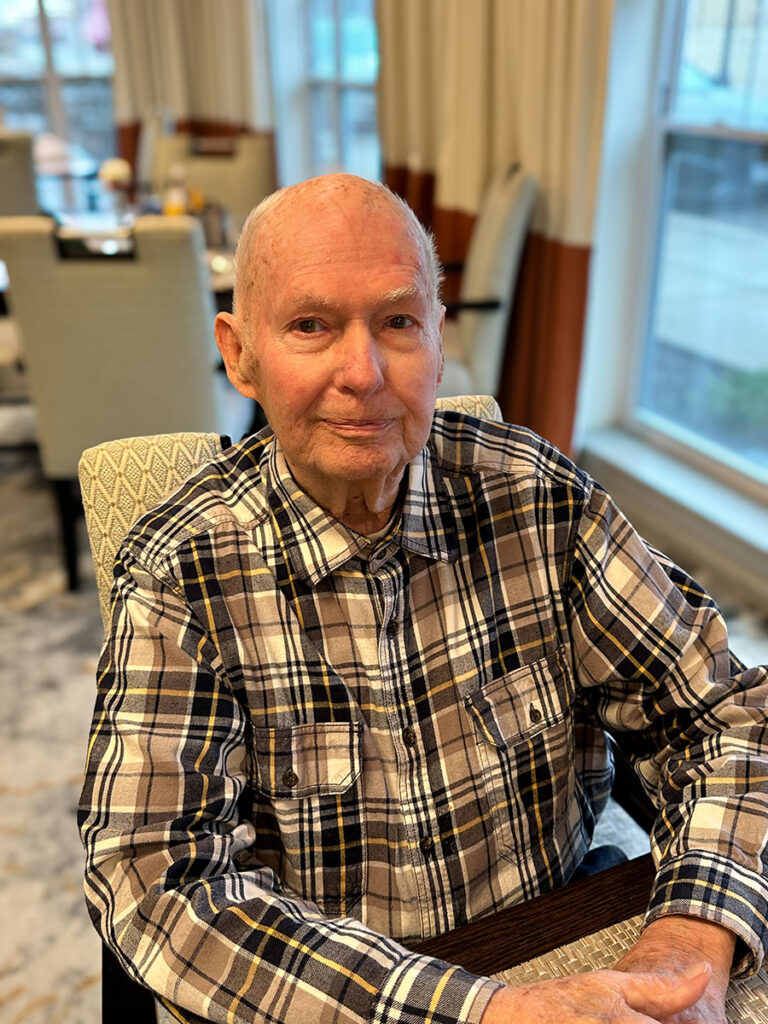 Senior resident sitting at a table in the community restaurant, smiling and chatting with friends.