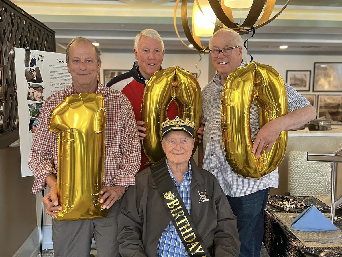 Three men holding a gold balloon that says 100, celebrating Verne's 