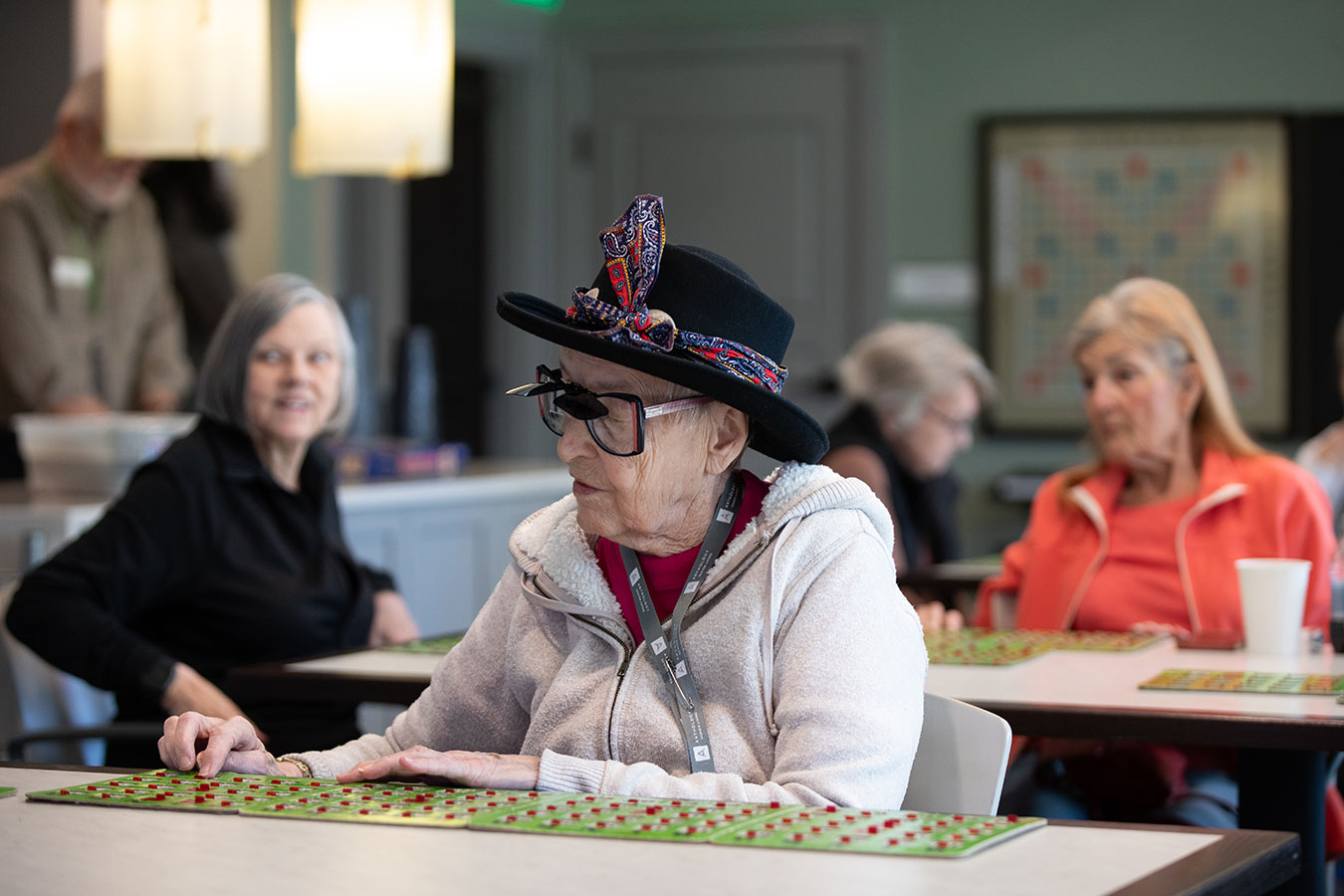 Elderly woman in hat and glasses playing board game at Bingo event, The Plaza at Wildwood senior living.