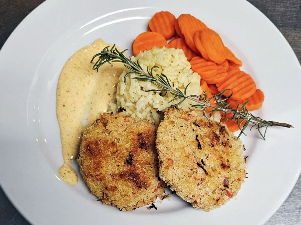 A white plate with Cajun style creole crab cakes, remoulade sauce, and rice pilaf.