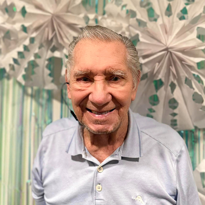 A senior resident smiling warmly in front of a winter-themed backdrop with paper snowflakes, radiating joy during a holiday celebration.